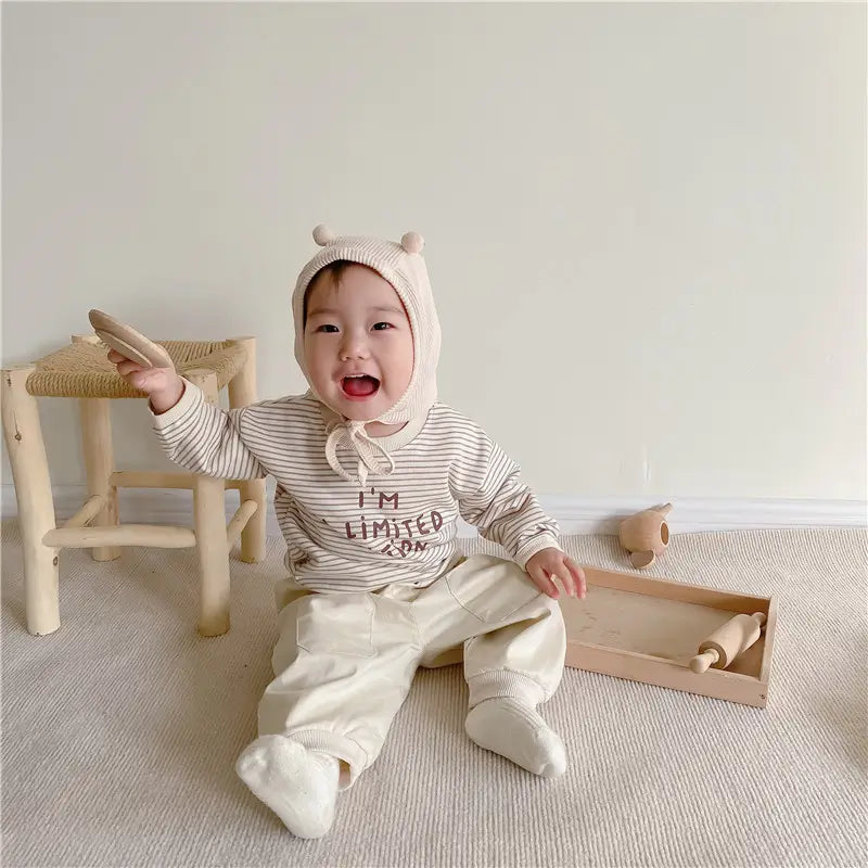 Baby girl wearing pink striped long sleeve top and beige trousers with bear hood